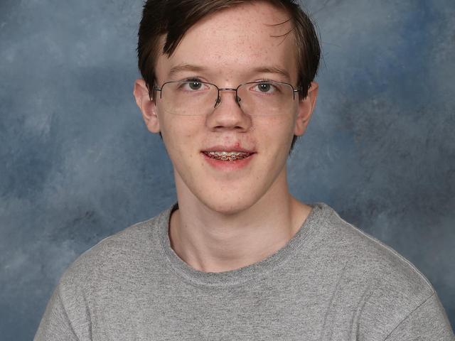 Thomas Matthew Crooks appears in this undated photo from his time at Bethel Park High School. Hes wearing glasses, braces on his teeth and a gray T-shirt that has an American flag and Mount Rushmore on it. Hes photographed against a gray backdrop.