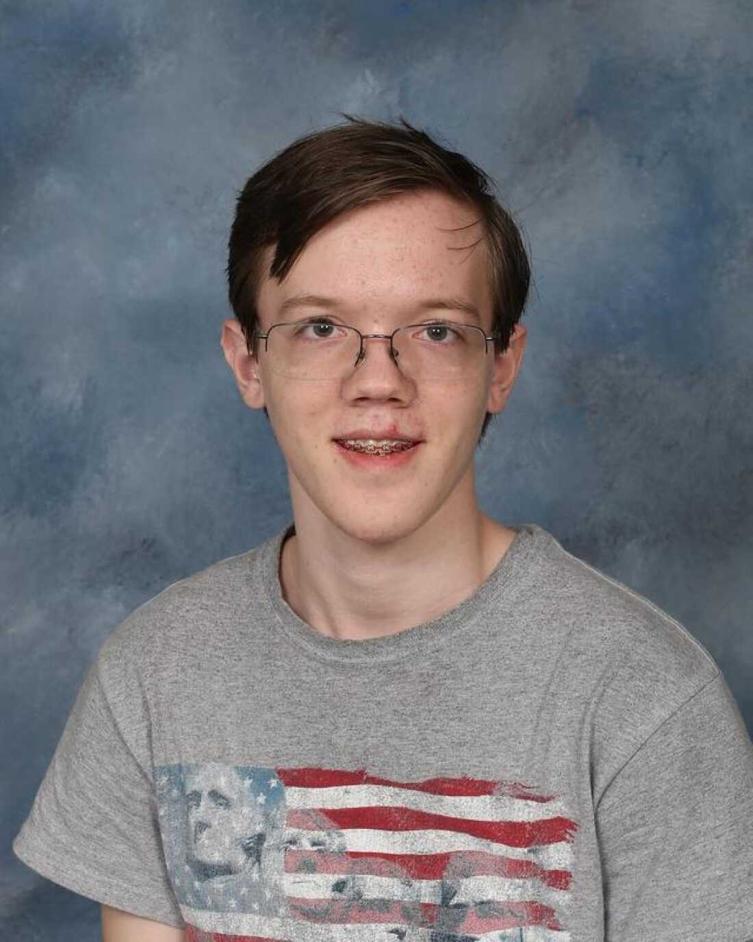 Thomas Matthew Crooks appears in this undated photo from his time at Bethel Park High School. He's wearing glasses, braces on his teeth and a gray T-shirt that has an American flag and Mount Rushmore on it. He's photographed against a gray backdrop.