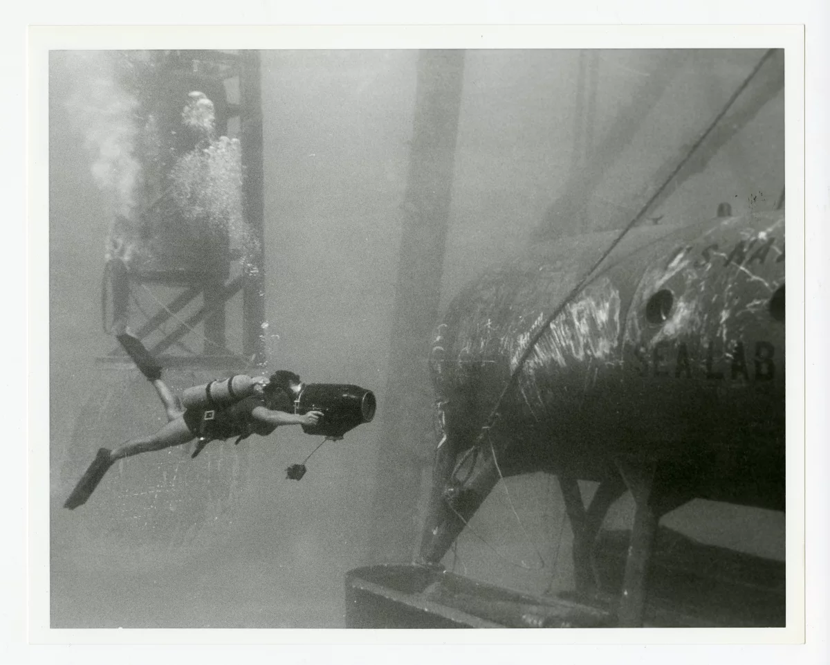 A Navy photographer films the Sealab I habitat.