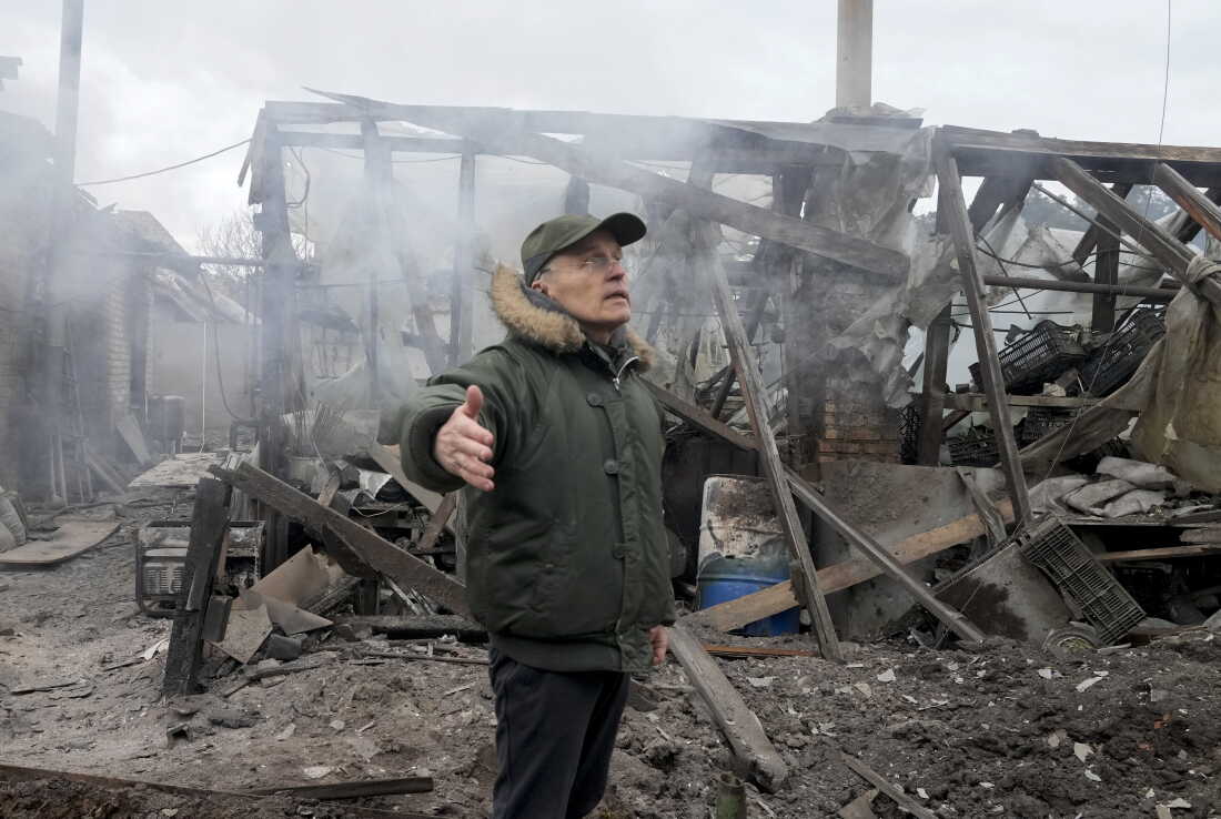A man stands with one arm extended out to his side near a house destroyed in Russian artillery shelling in the Kyiv suburb of Horenka on March 6, 2022.