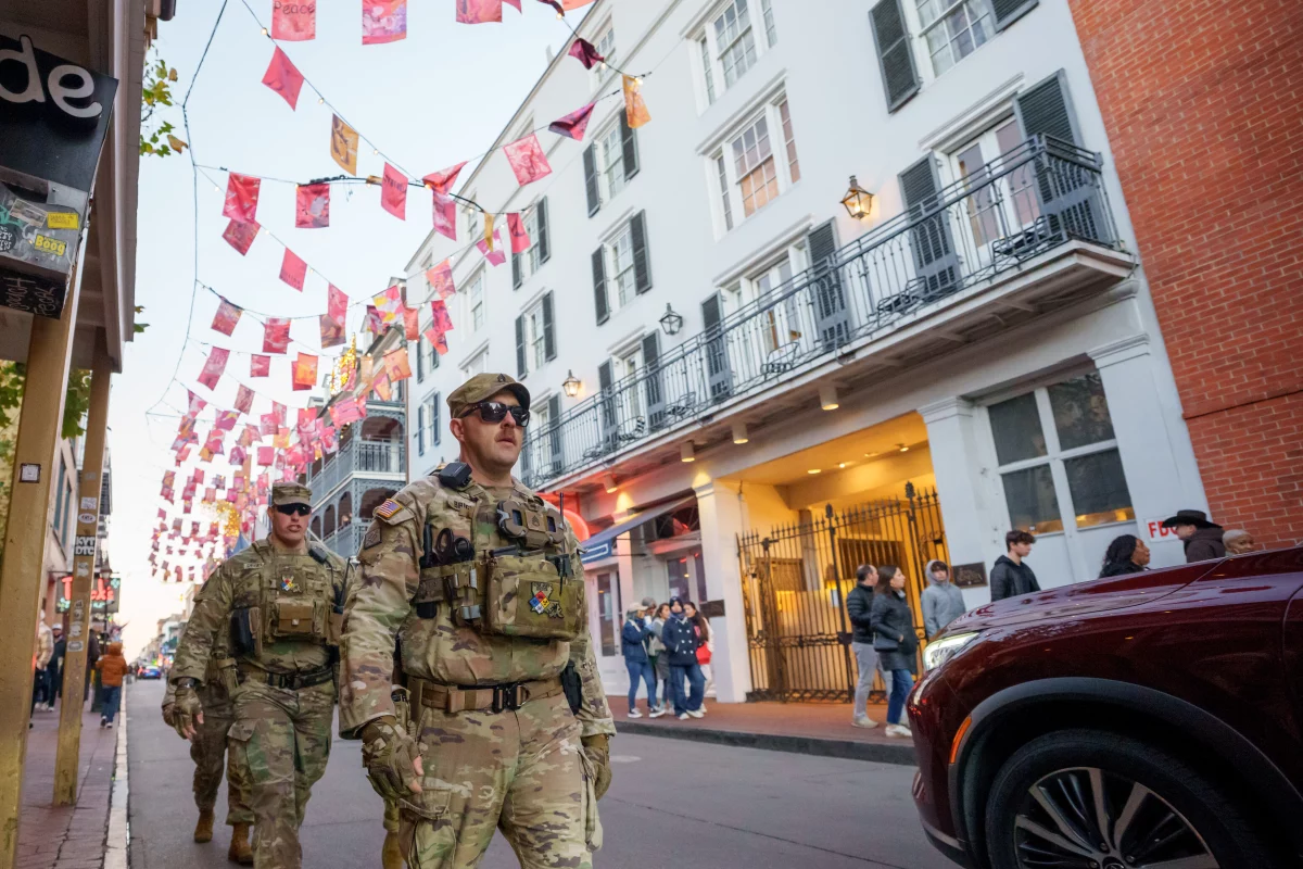 Walking under flags that memorialize victims of Jan. 1, 2025 attack, members of the Louisiana National Guard, military police, and Louisiana law enforcement agencies patrol the French Quarter along Bourbon Street and intersecting streets as part of a National Guard deployment for New Year's celebrations in New Orleans, Tuesday, Dec. 30, 2025. (AP Photo/Matthew Hinton)