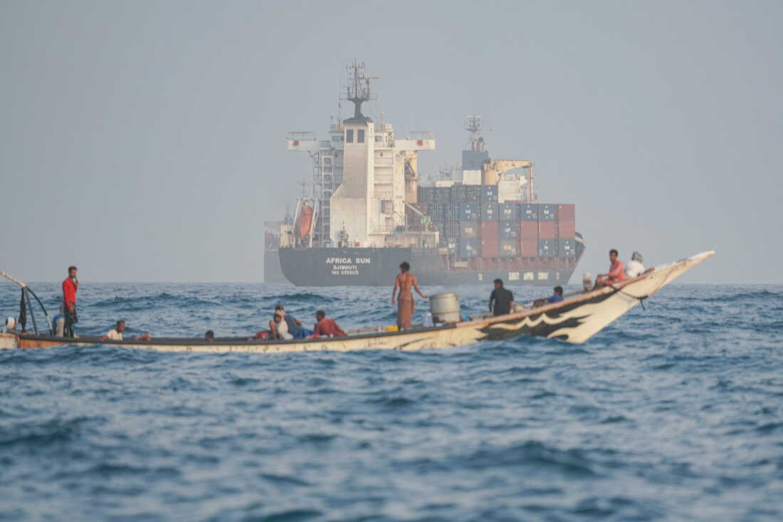 People sail their boat past container ships anchoring near the Strait of Bab al-Mandeb off Yemen's coast in the Gulf of Aden on Aug. 6, 2026.