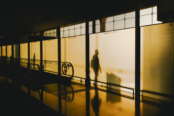 A photograph showing a moving walkway in an airport with beautiful, morning buttery light and a silhouette of a person stepping off the moving walkway.