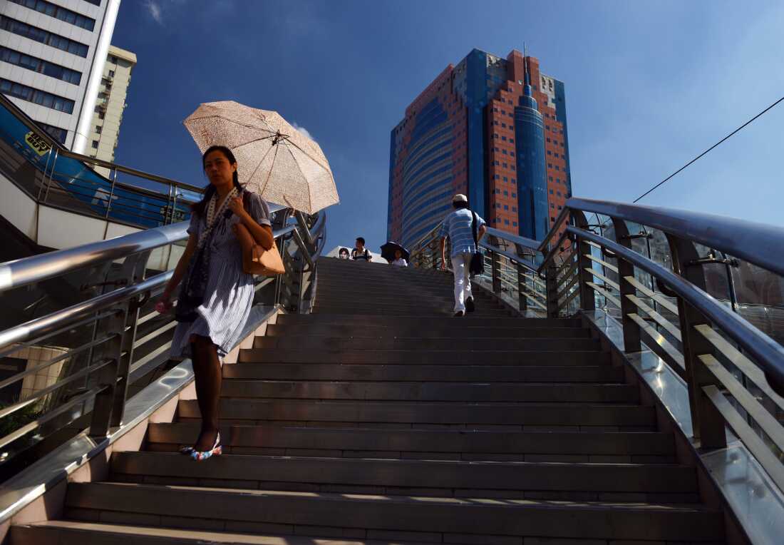 A woman uses an umbrella as a sun shade in August 2013 as she walks on an overpass in Shanghai, which was experiencing its worst heat in 140 years. A new study found that more than 200 heat waves, including the China heatwave, were substantially more likely and more intense because of the activity of major fossil fuel producers.