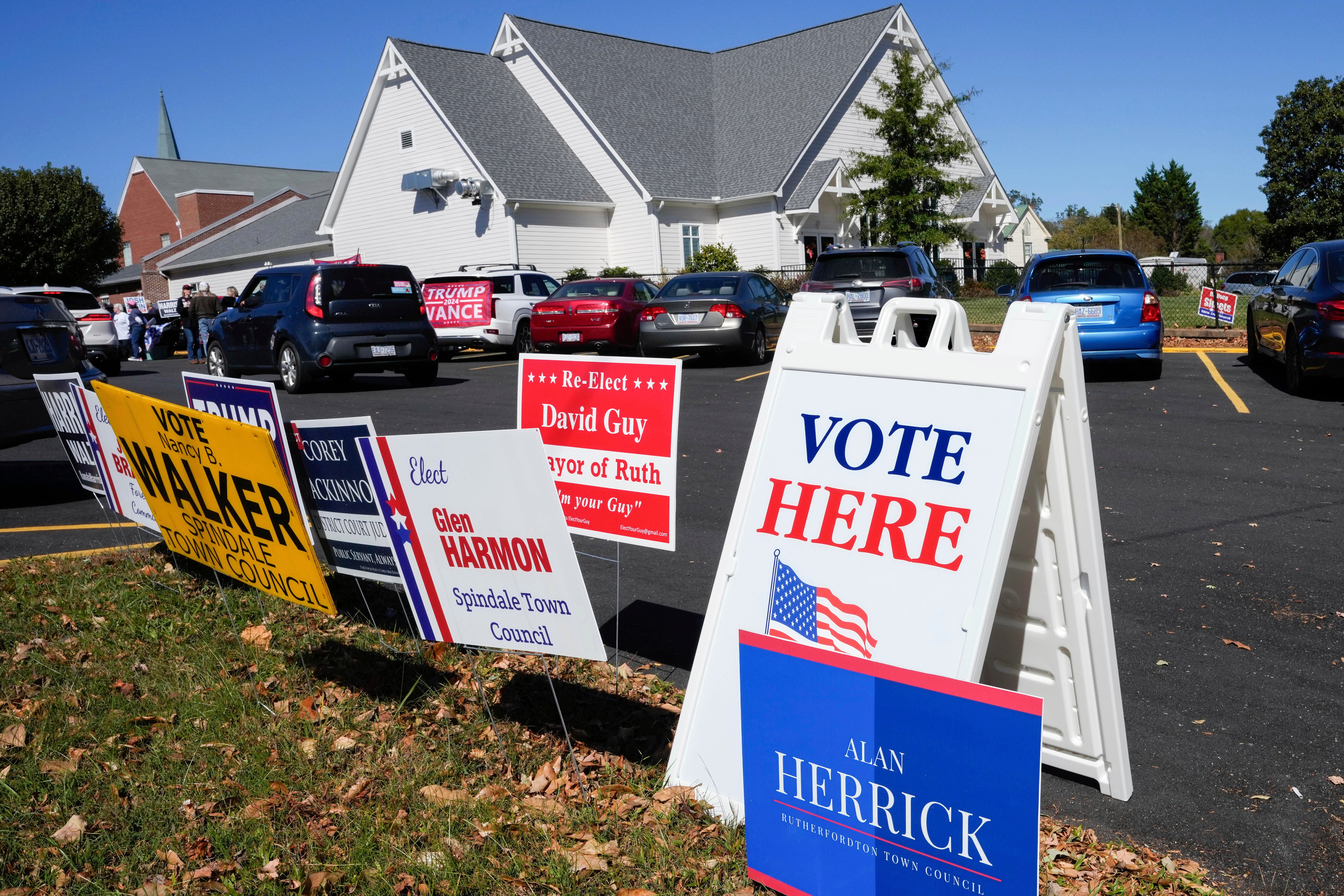 A Vote Here sign is posted amongst political signs as people arrive to vote at the Rutherford County Annex Building, an early voting site, Oct. 17, 2024, in Rutherfordton, N.C.