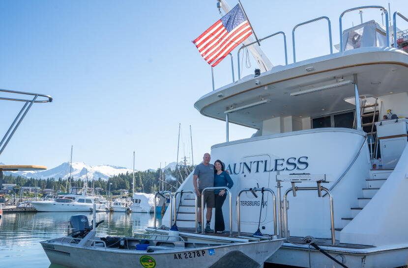 Jim Edgars and Alisa Jestel, the owner-operators of the Dauntless, stand below an American flag flying from the aft deck of their 92-foot motor yacht.