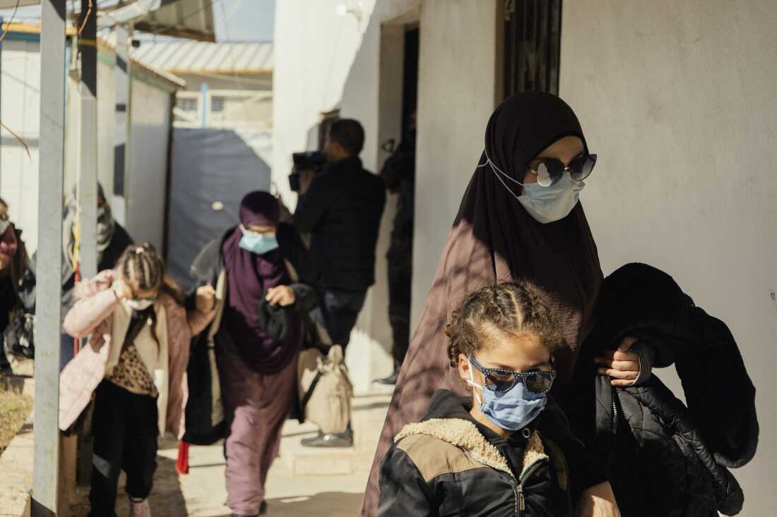 Women and children wearing sunglasses and face masks walk along a path before departure inside the Roj camp in al Malikiyah, Syria, on Feb. 15. These families, who had been affiliated with the Islamic State, are among 11 Australian families repatriated from the Roj camp. The transfer operations faced challenges and obstacles, leading to the families being returned to the camp until the issue is resolved.