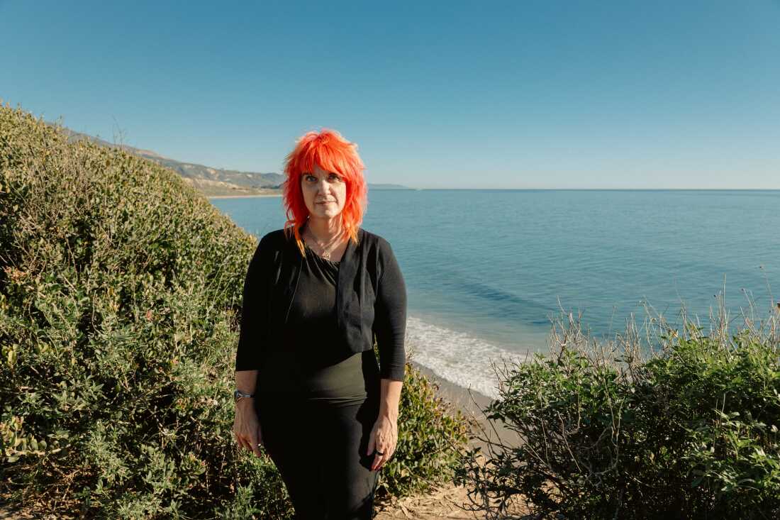 Small looks at the camera with the beach and Pacific Ocean behind her.
