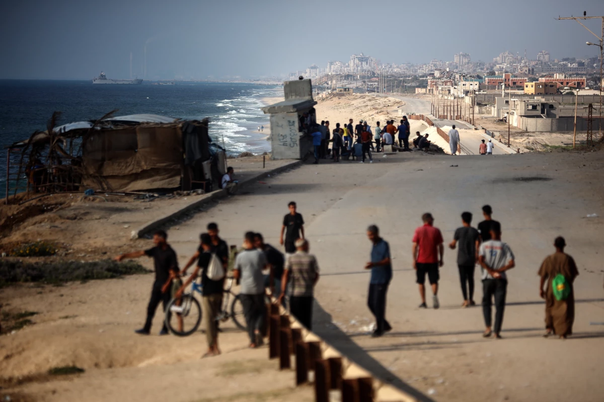 People watch a ship off the coast of Gaza near a temporary floating pier anchored by the United States to boost aid deliveries, as seen from the central Gaza Strip on June 27, 2024.