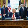 President Trump sits at a wooden desk at the White House as he speaks to the press. Behind him stand (from the left to right side of the frame) Attorney General Pam Bondi, Vice President Vance, Defense Secretary Pete Hegseth and Secretary of Homeland Security Kristi Noem.