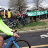 A cyclist rides on the asphalt past a group of people holding a protect our bike lane banner.