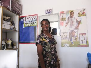 Maria da Graça Santos, the mother of Cape Verde national football team player, Ianique dos Santos Tavares— better known by his nickname, Stopira, in front of a poster of her son. At one of her shops in the capital, she sells Cape Verde football gear.