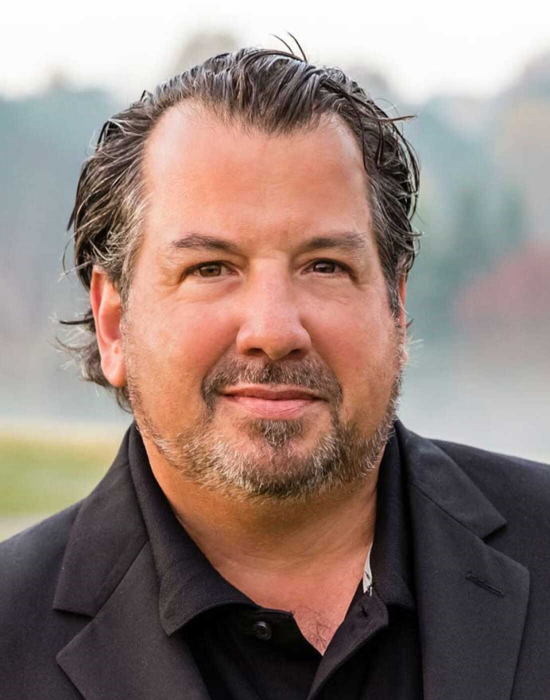 This photo is a headshot of Eric Wilhelm, who's wearing a black shirt and blazer.