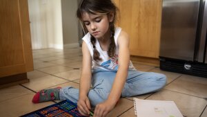 Second grader Augusta Robbins sits on the floor drawing at the temporary Airbnb her family was staying in. Since her family home burned down, she’s been drawing a lot of houses.