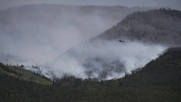A helicopter drops water on the Cottonwood Fire in Beaver, Utah. White smoke fills the air. 