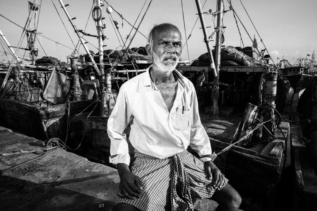 Nandu Kumar, 65, sits among fishing boats at Kasimedu Fishing Harbour in Chennai, India. A former fisherman who now sells fish on shore, Kumar says he once smuggled imported alcohol and cigarettes to make a living.