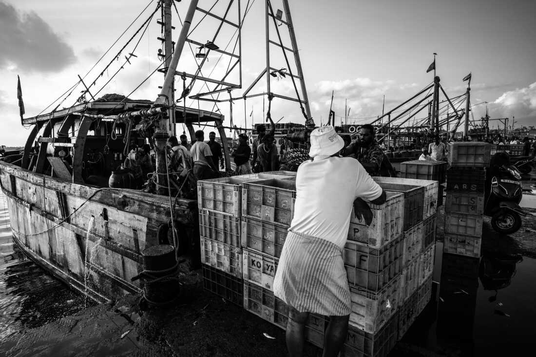 Workers gather beside a fishing boat and stacks of plastic crates at Kasimedu Fishing Harbour in Chennai, India. Built for fewer than 600 boats, the harbor now serves far more vessels and workers each day.