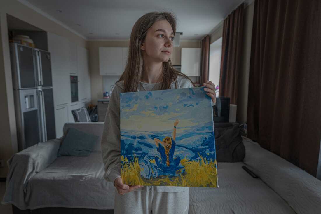 Alona Serdiuk, 23, an IDP from Komysh Zoria, Zaporizhzhia region holds her painting in Ukrainian's flag colors at parents' home in Zaporizhia.