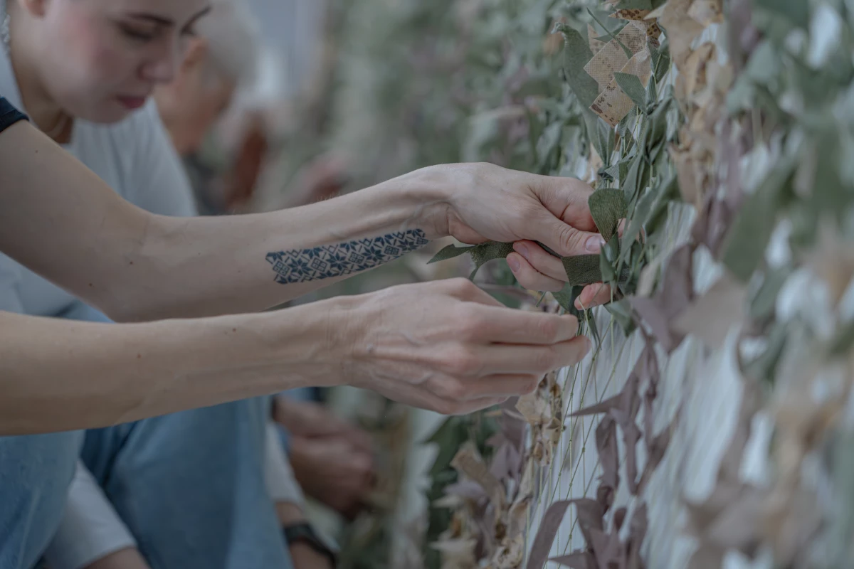 Kateryna Kyshkan weaves strips of cloth into camouflage netting. She worried that her patriotic Ukrainian tattoo would get her arrested at Russian checkpoints.