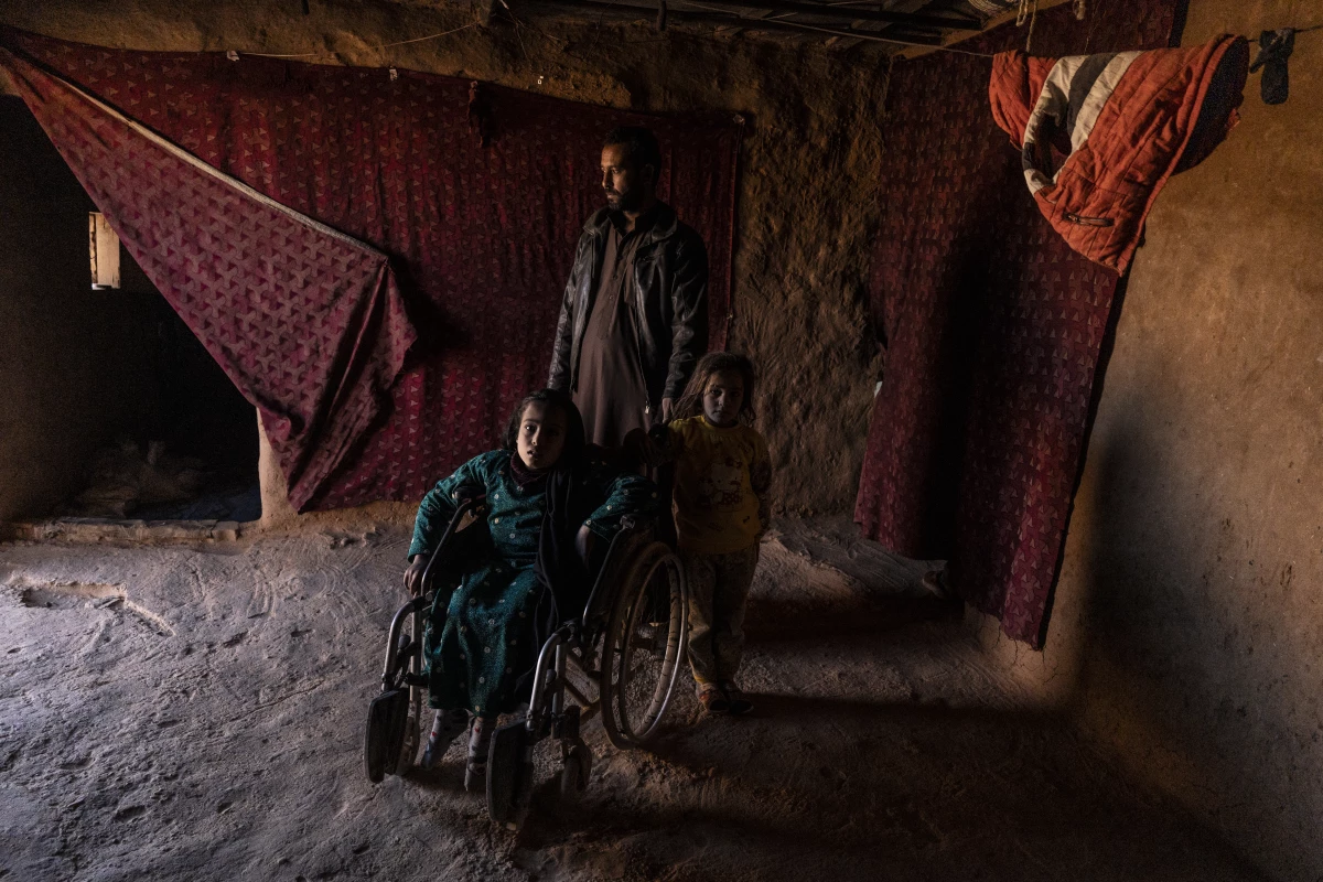 She'ala Hjab Khaled sits in a wheelchair, with her father and sister standing with her, in their house in the Rukban camp for displaced people in southern Syria, Dec. 14.