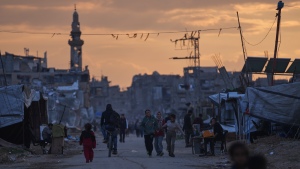 Palestinian youth walk along a tent camp for displaced people as the sun sets in Nuseirat, central Gaza Strip, Friday, Dec. 26, 2025.