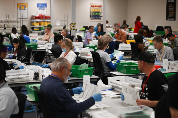 Pairs of election workers from different political parties open and inspect mail ballot envelopes inside the Maricopa County Tabulation and Election Center in Phoenix on Election Day, Nov. 5, 2024.