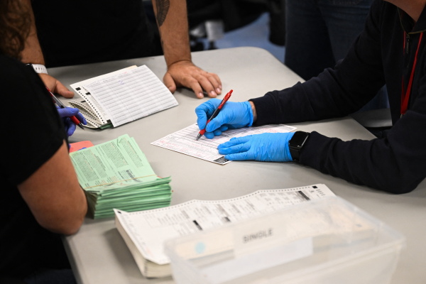 Pairs of election workers from different political parties open and inspect mail ballot envelopes inside the Maricopa County Tabulation and Election Center in Phoenix on Election Day, Nov. 5, 2024.