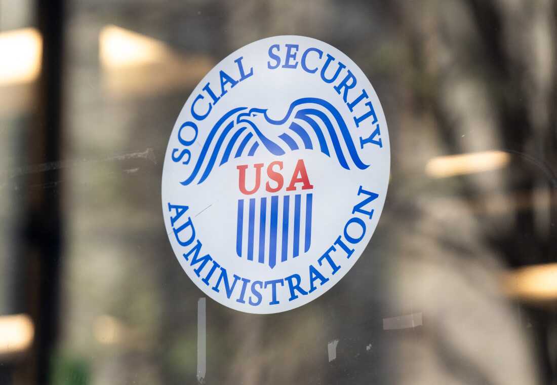 This photo shows the Social Security Administration logo on a glass window of a Social Security Administration office in Washington, D.C., in March. The round white logo features a blue eagle, the letters "USA" in red in the middle and the words "SOCIAL SECURITY ADMINISTRATION" in blue around the border of the circle.