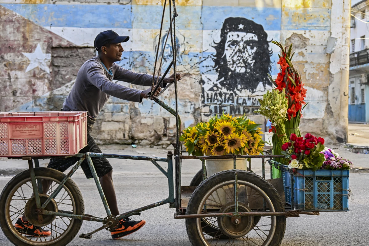 A flower street vendor pushes his cart past a mural depicting Argentine-born revolutionary leader Ernesto 'Che' Guevara reading 'Until victory, always.' in Havana on Feb. 25, 2026. The US-imposed oil blockade on Cuba is upending the lives of everyday workers, who are switching jobs and ditching their cars to make do amid rolling blackouts and fuel shortages.