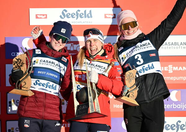 Three female skiers wearing winter gear hold trophies.