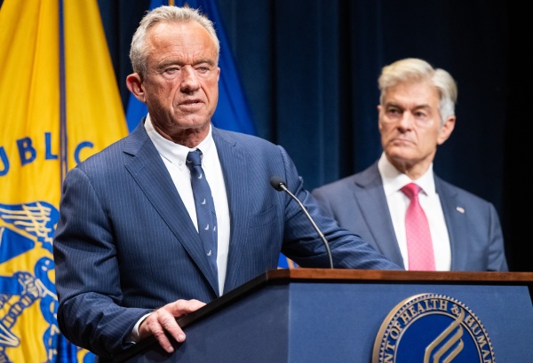Secretary of Health and Human Services Robert F. Kennedy Jr. addresses reporters on Monday as Medicare and Medicaid Administrator Dr. Mehmet Oz (R) listens. The two men are seen behind a podium that has the HHS logo on it.