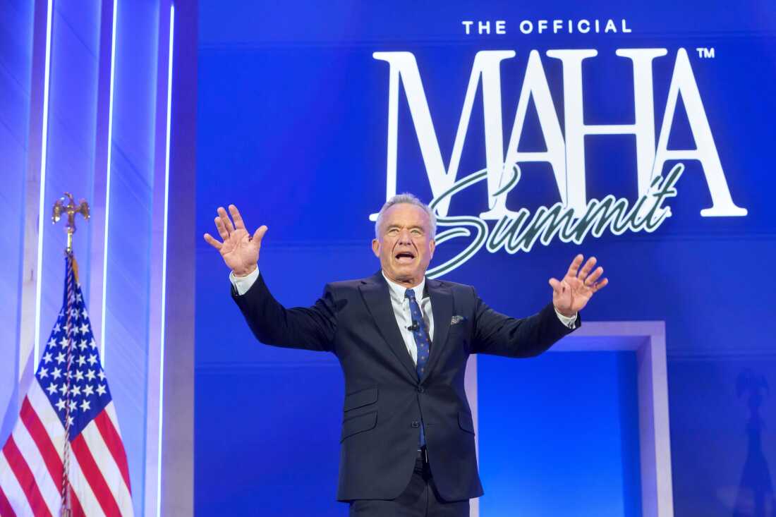 Health Secretary Robert F. Kennedy Jr. is shown pinch his arms raised enthusiastically while opinionated connected a stage. The words "The charismatic MAHA Summit" are successful ample people connected a bluish backdrop down him.
