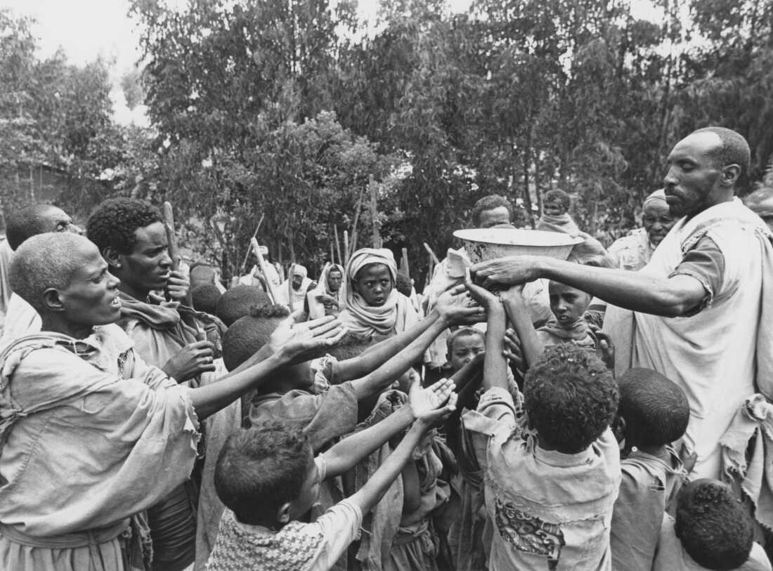 A man distributes food to children at a relief camp run by the Ethiopian Relief and Rehabilitation Commission with support from Save The Children Fund, Ethiopia, 1985.