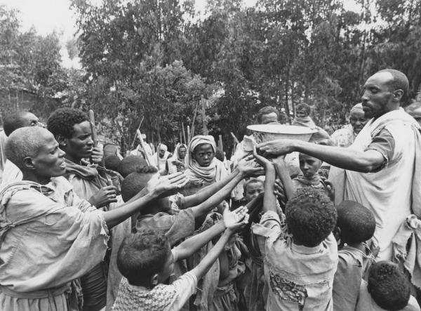 A man distributes food to children at a relief camp run by the Ethiopian Relief and Rehabilitation Commission with support from Save The Children Fund, Ethiopia, 1985.