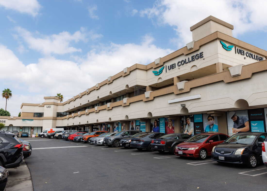 This photo shows the UEI College campus in Huntington Park, California. It's a long two-story building with a parking lot in front.