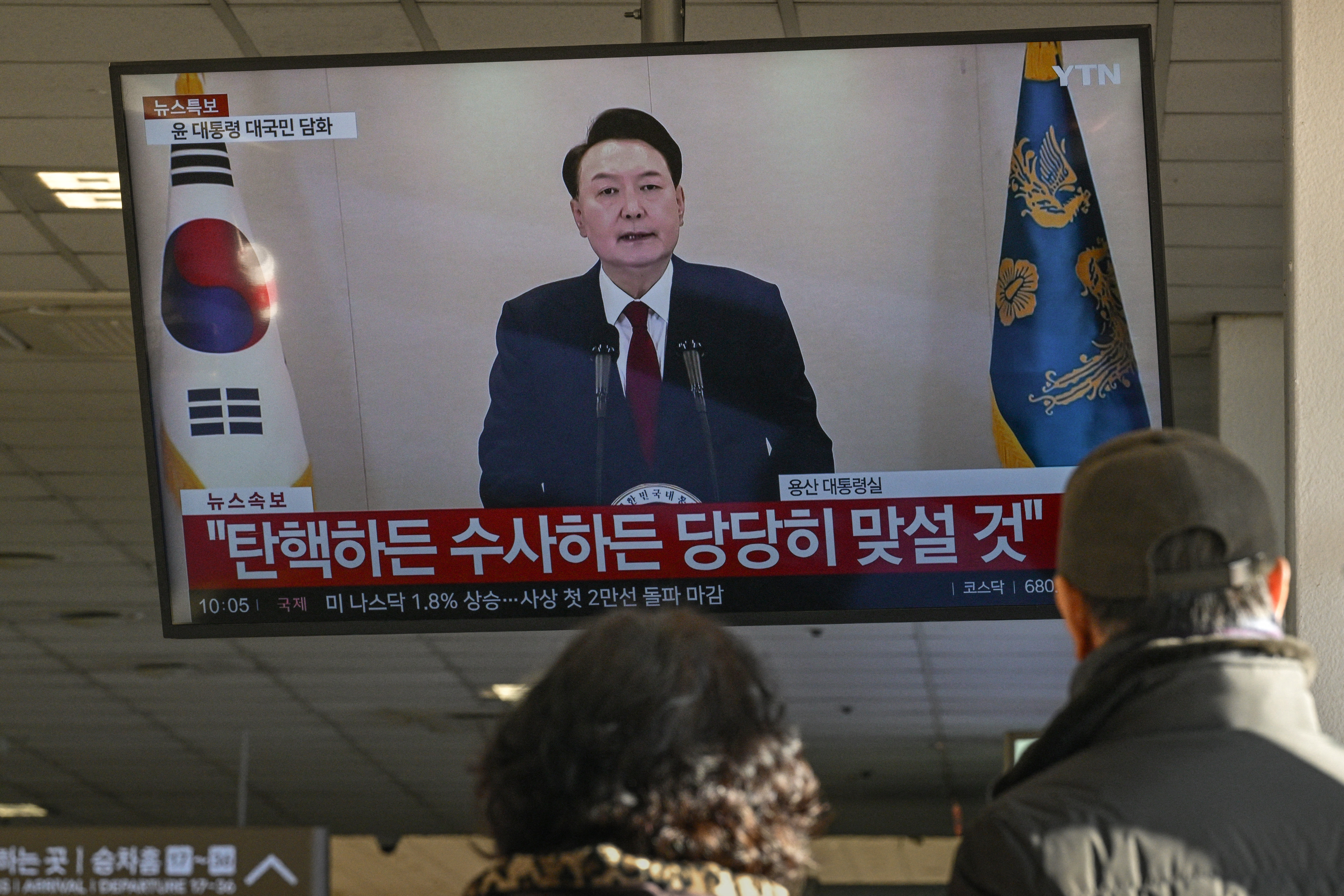 People watch a screen showing South Korean President Yoon Suk Yeol speaking during a televised address at a bus terminal in Seoul on Dec. 12, 2024.