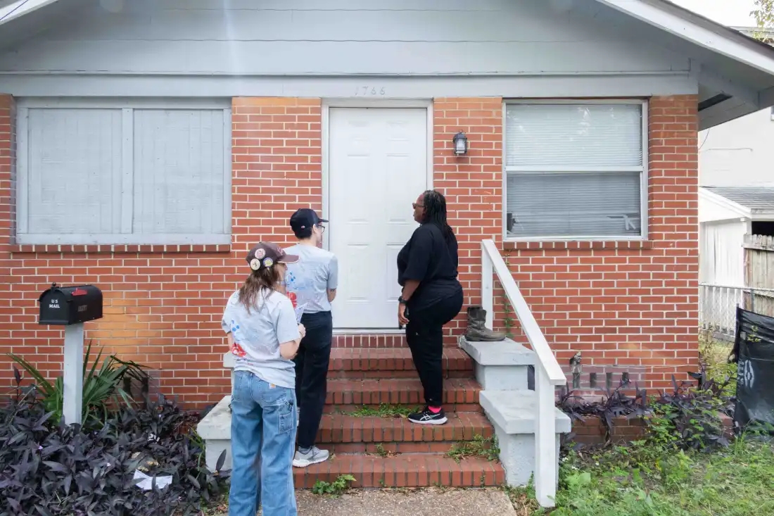 Three volunteers with Florida Rising stand outside the front door of a brick house in Jacksonville, Fla.