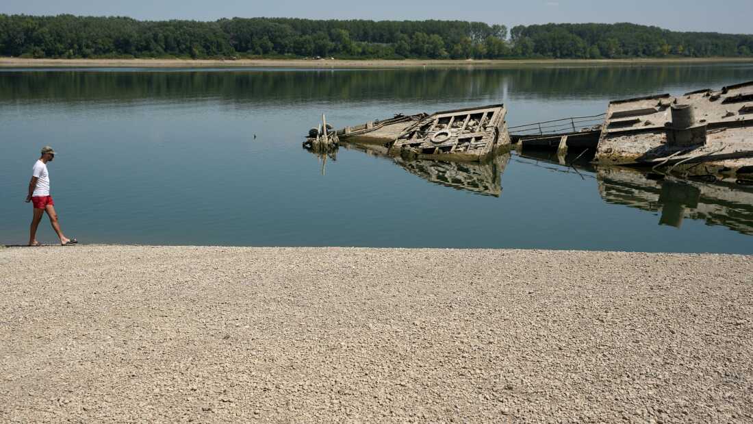 A man walks on the sandbank by the wreckage of a WWII German warship, emerged due to the drought, in front of Djerdap II, a large dam on the Danube River, between Romania and Serbia, near Prahovo, Serbia, Tuesday, Aug. 4, 2026.