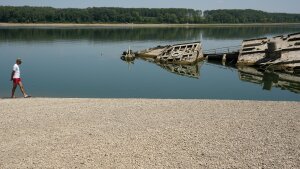 A man walks on the sandbank by the wreckage of a WWII German warship, emerged due to the drought, in front of Djerdap II, a large dam on the Danube River, between Romania and Serbia, near Prahovo, Serbia, Tuesday, Aug. 4, 2026.