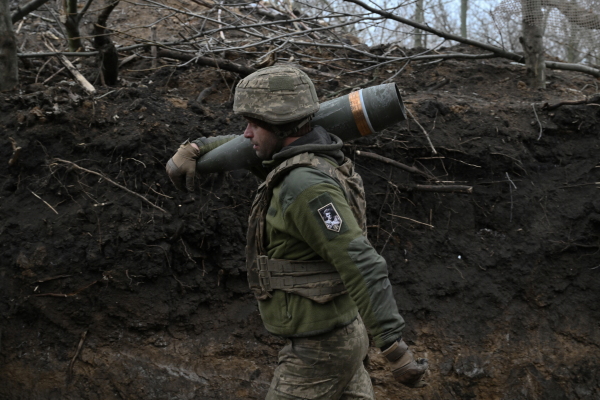 In this photo, an artilleryman wearing a camouflage-print uniform carries a self-propelled howitzer on his right shoulder, with his right arm holding it in place.
