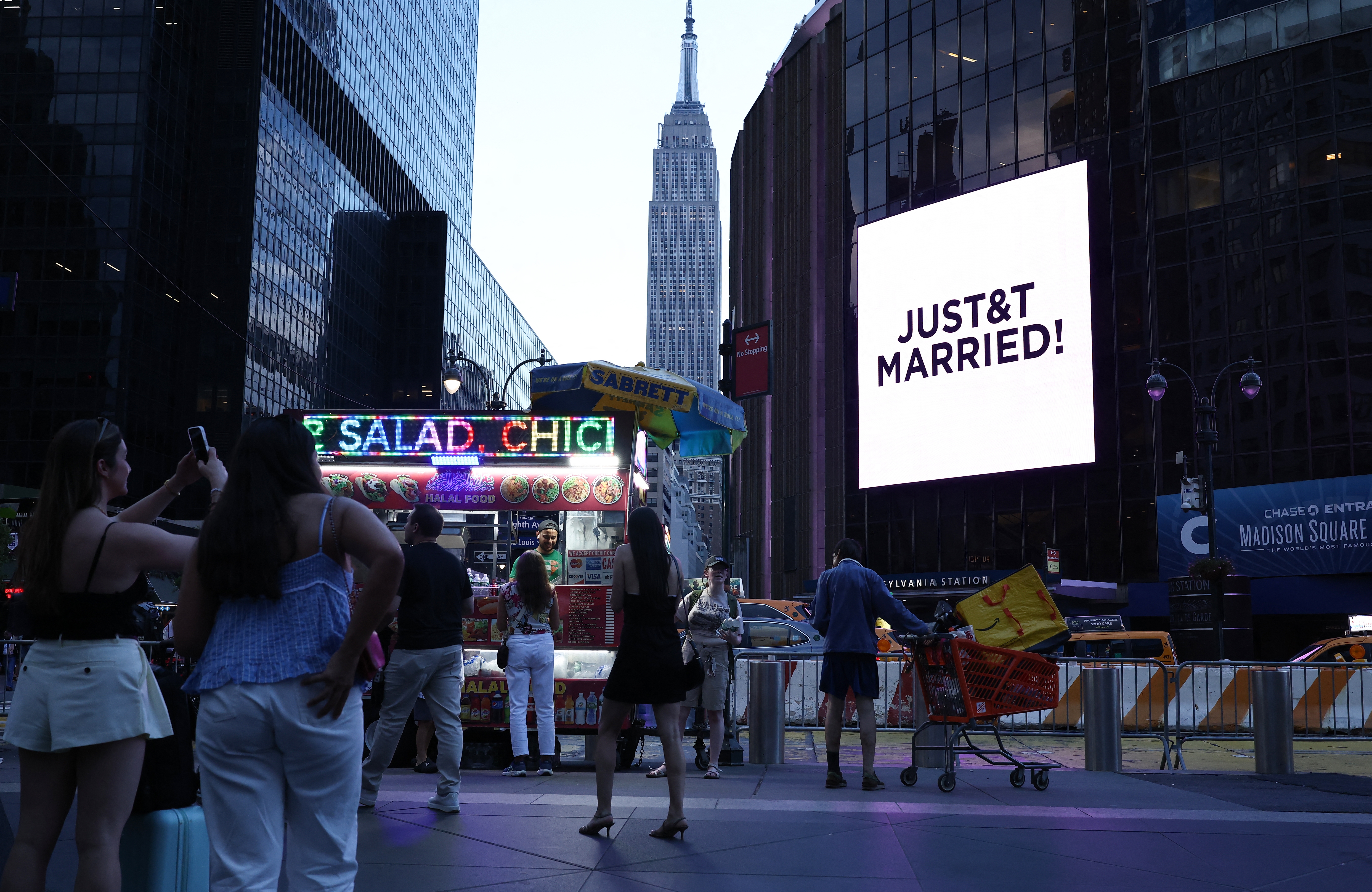The Empire State Building is seen in the distance as people take photos of a giant screen showing the message "JUST&T MARRIED!" (T&T for Taylor and Travis) outside Madison Square Garden, where wedding celebrations of pop singer Taylor Swift and Travis Kelce of the Kansas City Chiefs were held, in New York City on Friday.