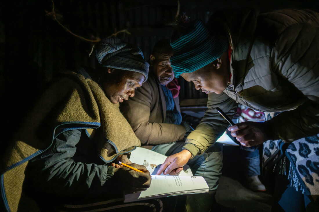 Teacher Mampho Makha assists a student during class at a shepherd night school in the village of Ha Ntsokoane in Thaba Tseka, Lesotho. The school is run on a shoestring budget and lacks electricity, so learning is carried out by phone light.