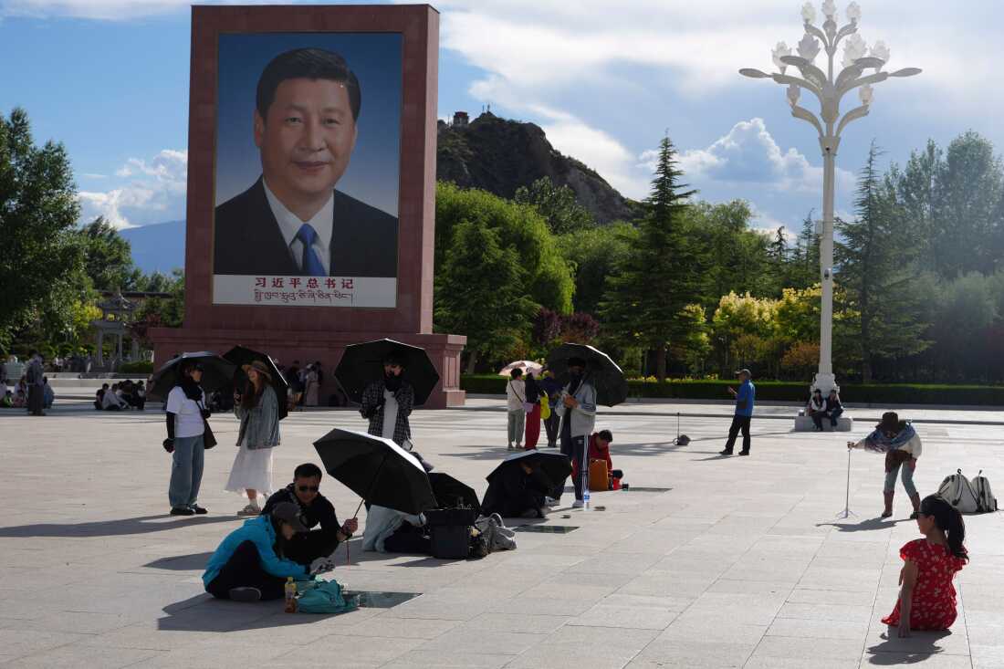 Tourists rest near a portrait of Chinese President Xi Jinping at a public square at the base of the Potala Palace in western China's Tibet autonomous region on July 21, 2026, during a government-organized visit for foreign journalists.