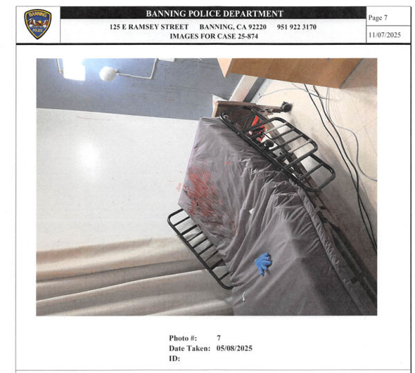 A hospital bed is shown, with light red stains near the head of the bed. The photo is framed labeled "Banning Police Department."