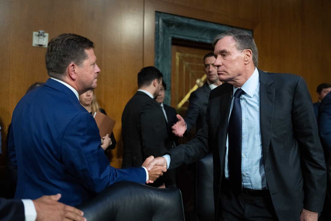 Jay Clayton, left, shakes hands with Sen. Mark Warner, D-Va., following his confirmation hearing for Director of National Intelligence on July 15, 2026. Warner says administration officials have failed to provide legally-mandated pre-election reports to Congress on foreign election meddling efforts.