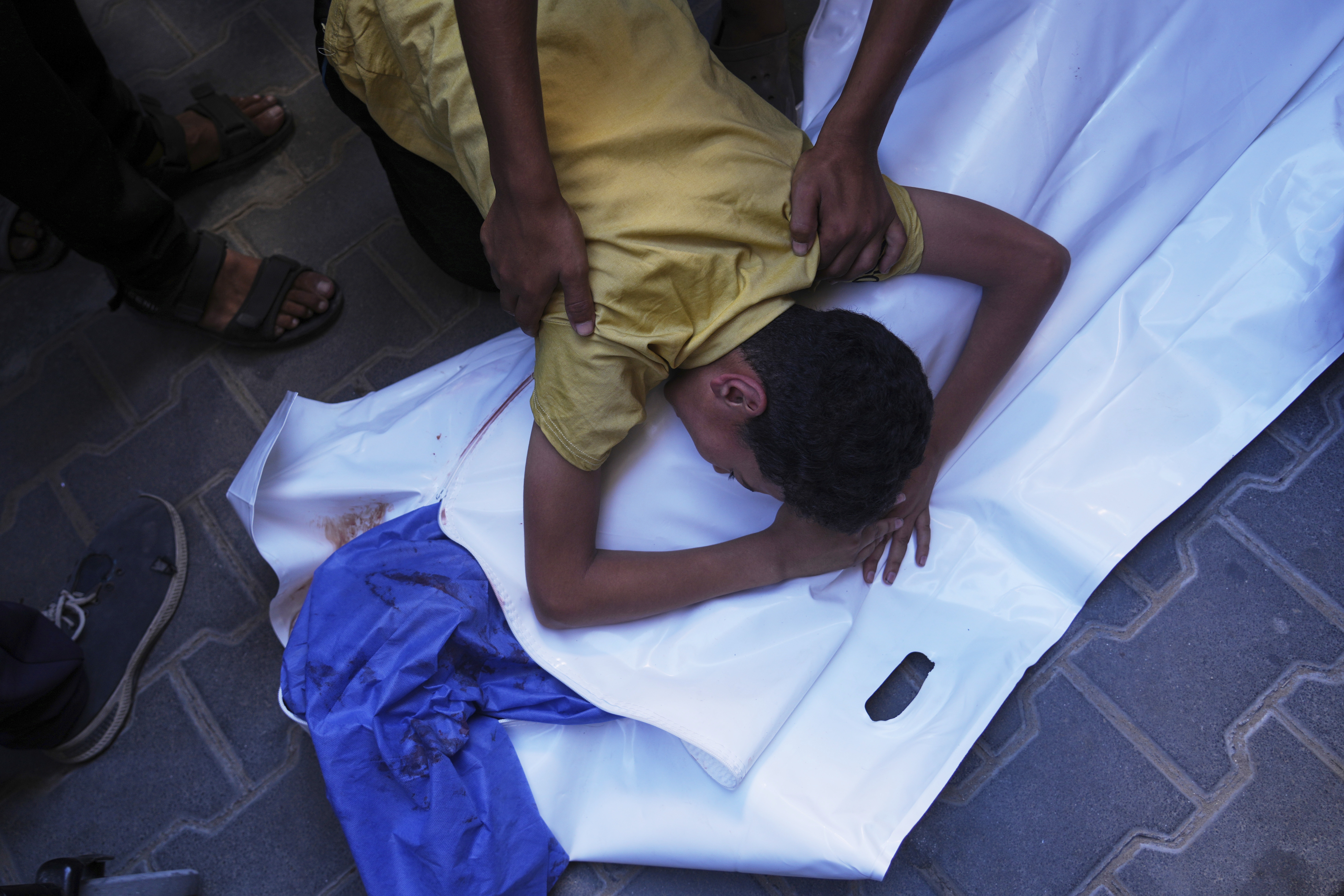 A Palestinian boy mourns over the body of his 12-year-old friend, Abdullah Ahmed, who was killed in an Israeli strike that targeted a drinking water distribution point, at Al-Awda Hospital in Nuseirat, central Gaza Strip, Sunday, July 13, 2025.