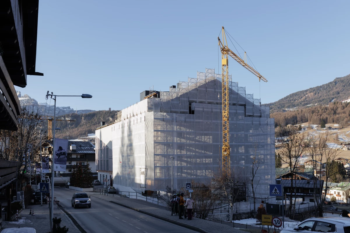 A construction crane towers over a building wrapped in scaffolding in the center of Cortina d'Ampezzo. The town is currently undergoing a massive urban transformation with more than 20 cranes dotting the landscape, as organizers work to complete approximately 98 approved infrastructure projects Games.