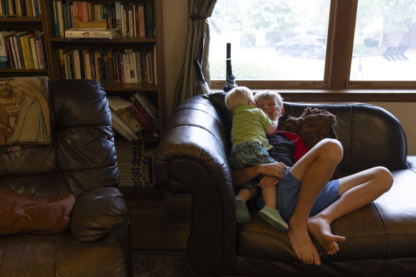 Dimitry and his youngest brother, Sven, are on a couch in a cuddly pose. In the background are windows and bookcases filled with books.