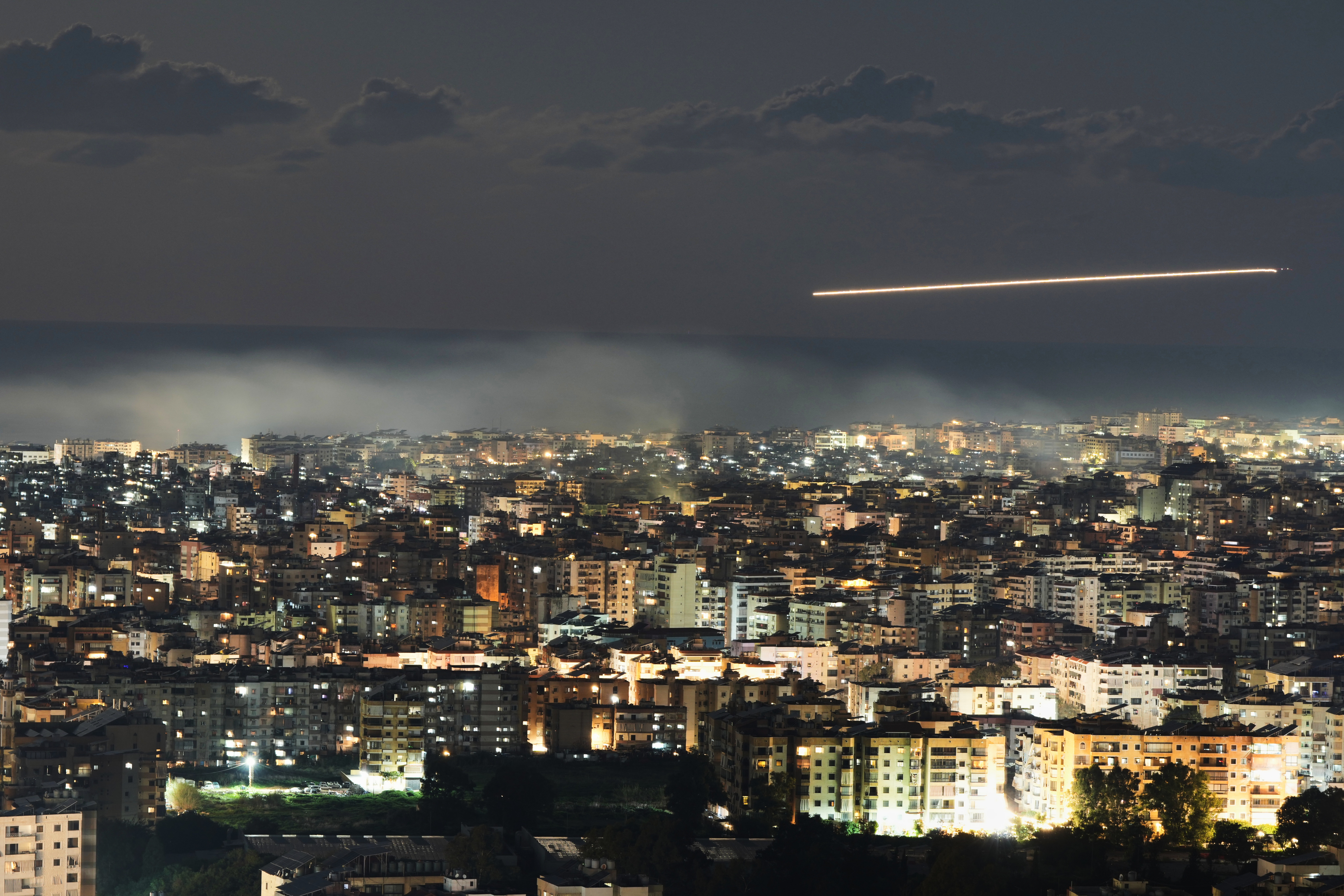 In this photo taken with a slow shutter speed, a Middle East Airlines plane flies over Beirut as smoke rises from Israeli airstrikes on Dahiyeh in Beirut
