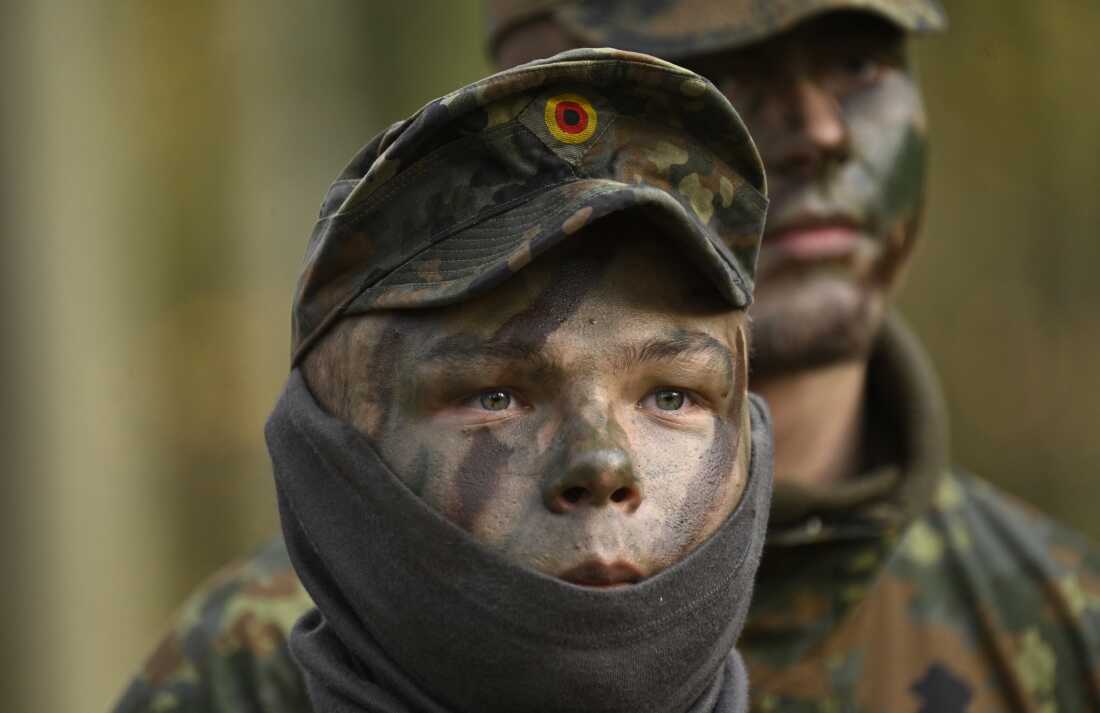 Two German recruits, wearing camouflage face paint and camouflage-print uniforms, attend a tank destruction exercise at the Westfalen-Kaserne barracks of the German armed forces on November 13, 2025. They are photographed from about the shoulders up.